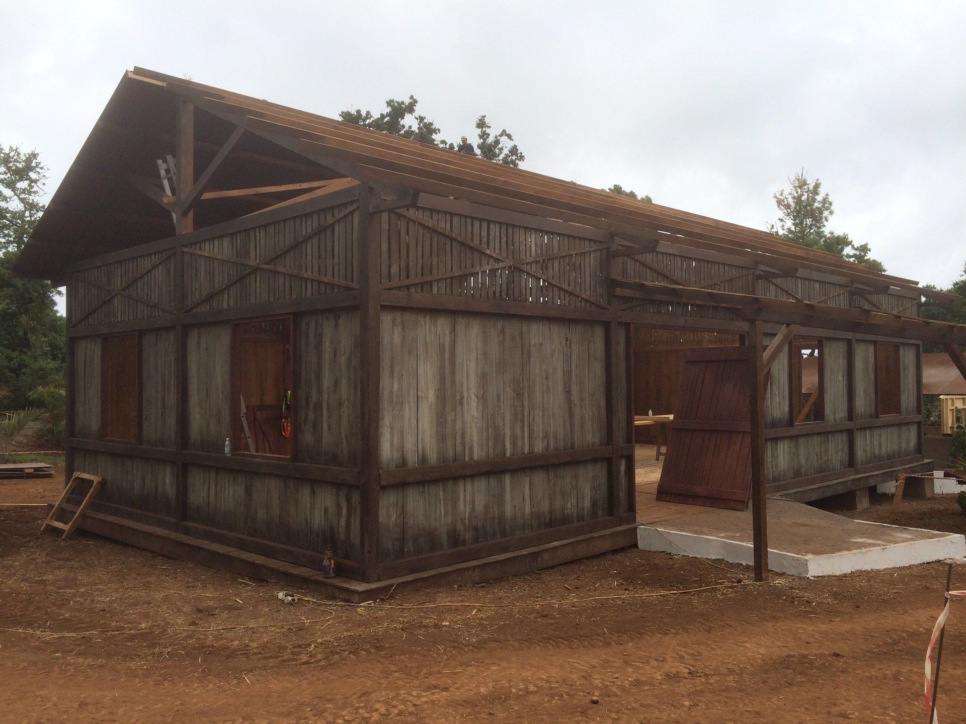 Un gran edificio de madera con techo de tejas rojas está ubicado encima de un campo de tierra.