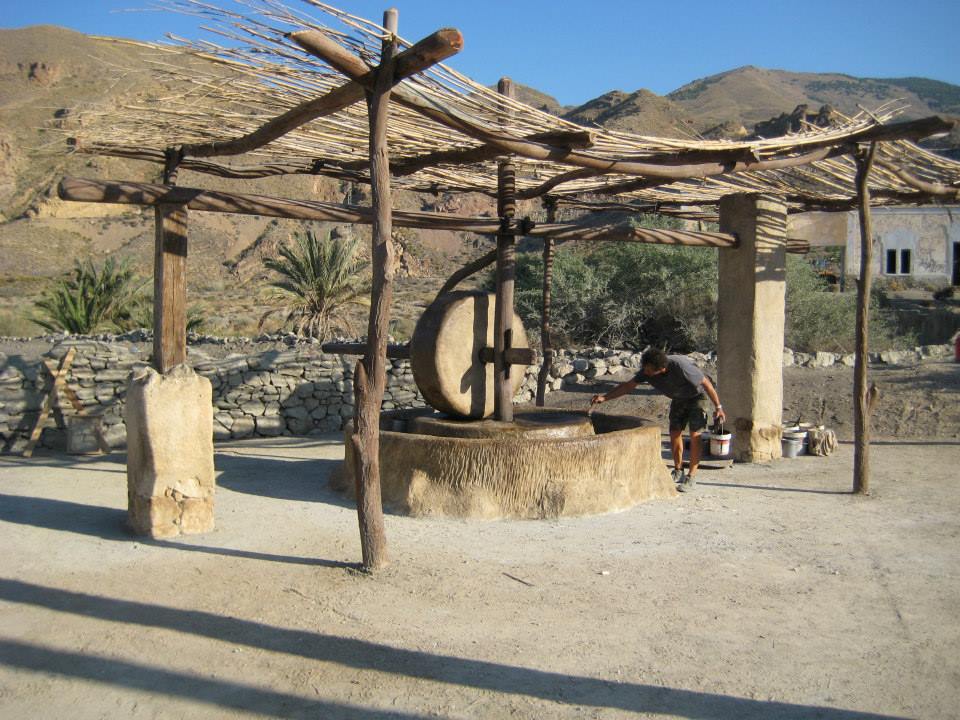Un hombre se sienta debajo de una estructura de madera junto a un pozo.