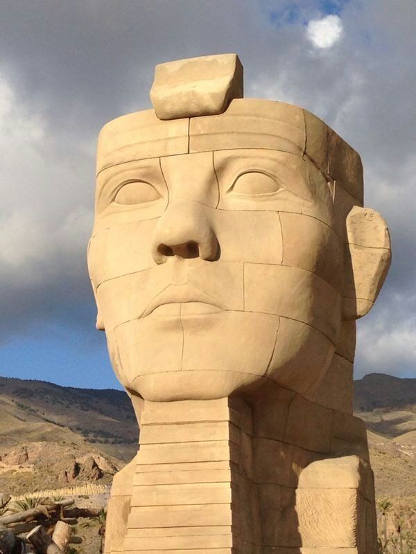 Un primer plano de una estatua de la cara de un hombre con montañas al fondo.