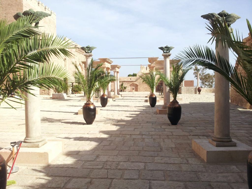 Un camino de piedra con palmeras y columnas.