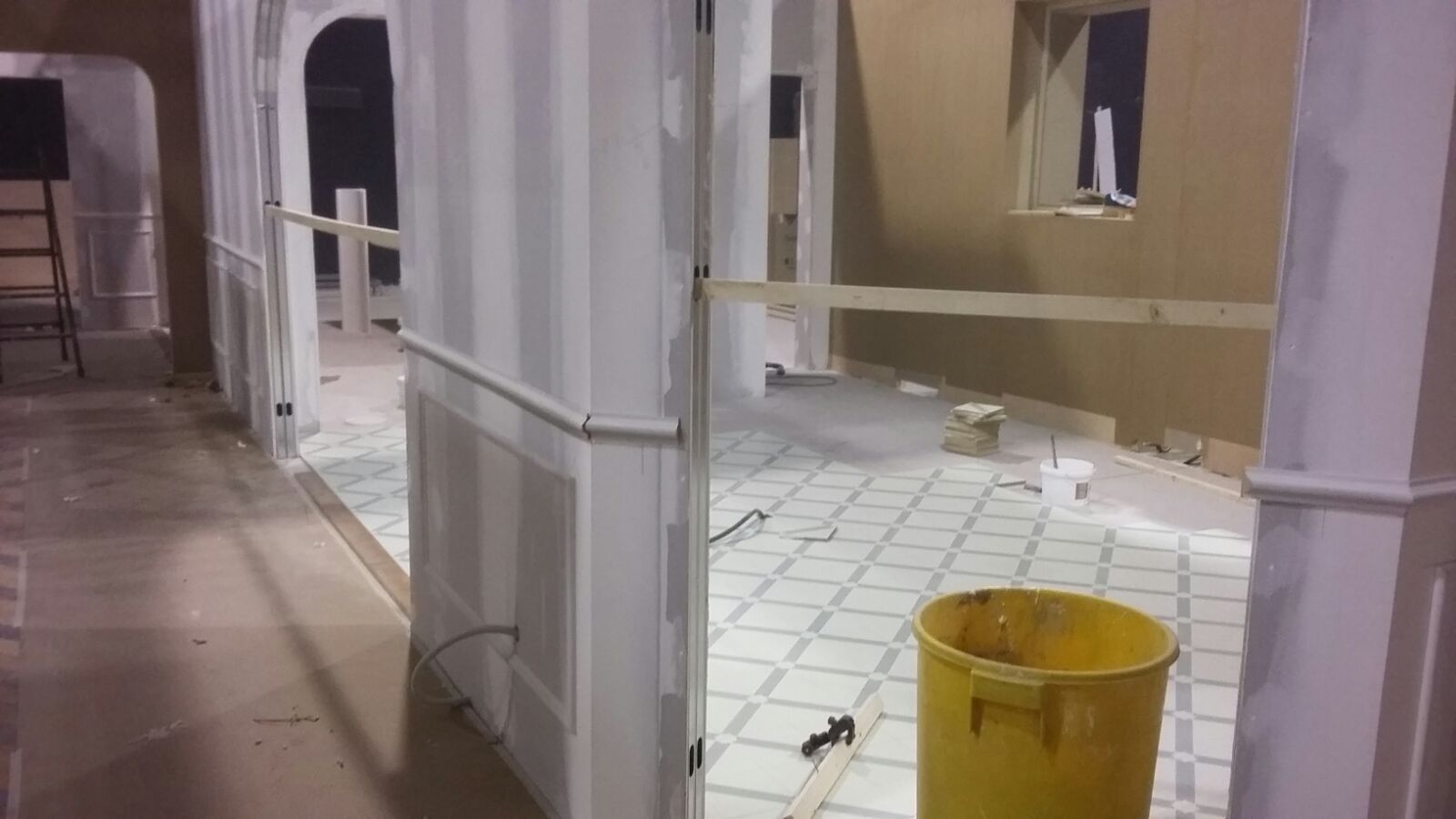 Un bote de basura amarillo está en un pasillo al lado de una pared.