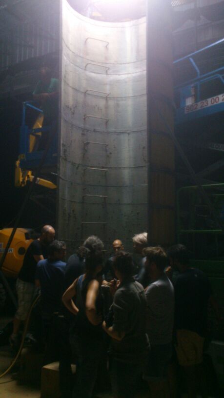 Un grupo de personas está de pie alrededor de un gran cilindro de metal en una habitación oscura.