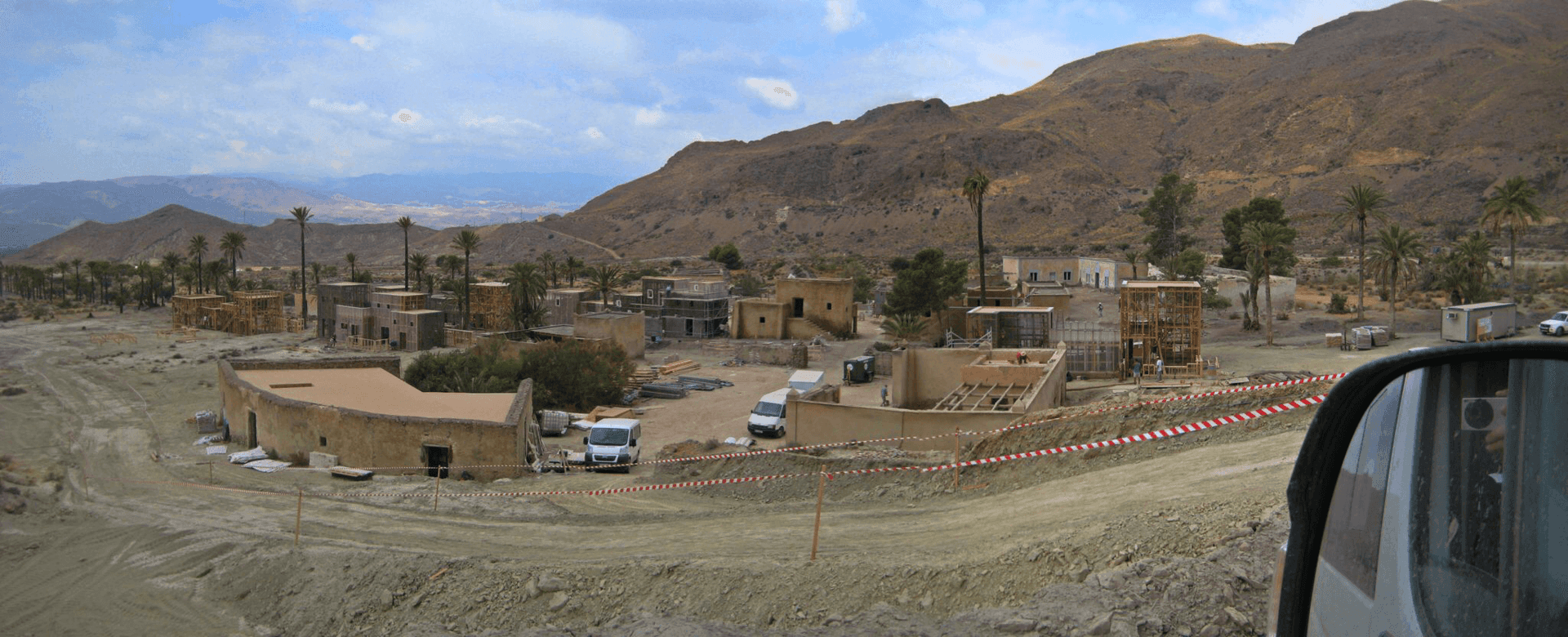 Un coche circula por un camino de tierra con montañas al fondo.