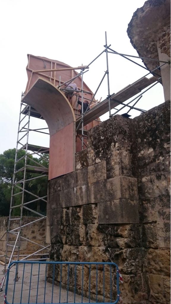 Un muro de piedra con andamios a su alrededor y una valla delante.