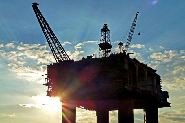 Una silueta de una plataforma petrolera con el sol brillando a través de las nubes.