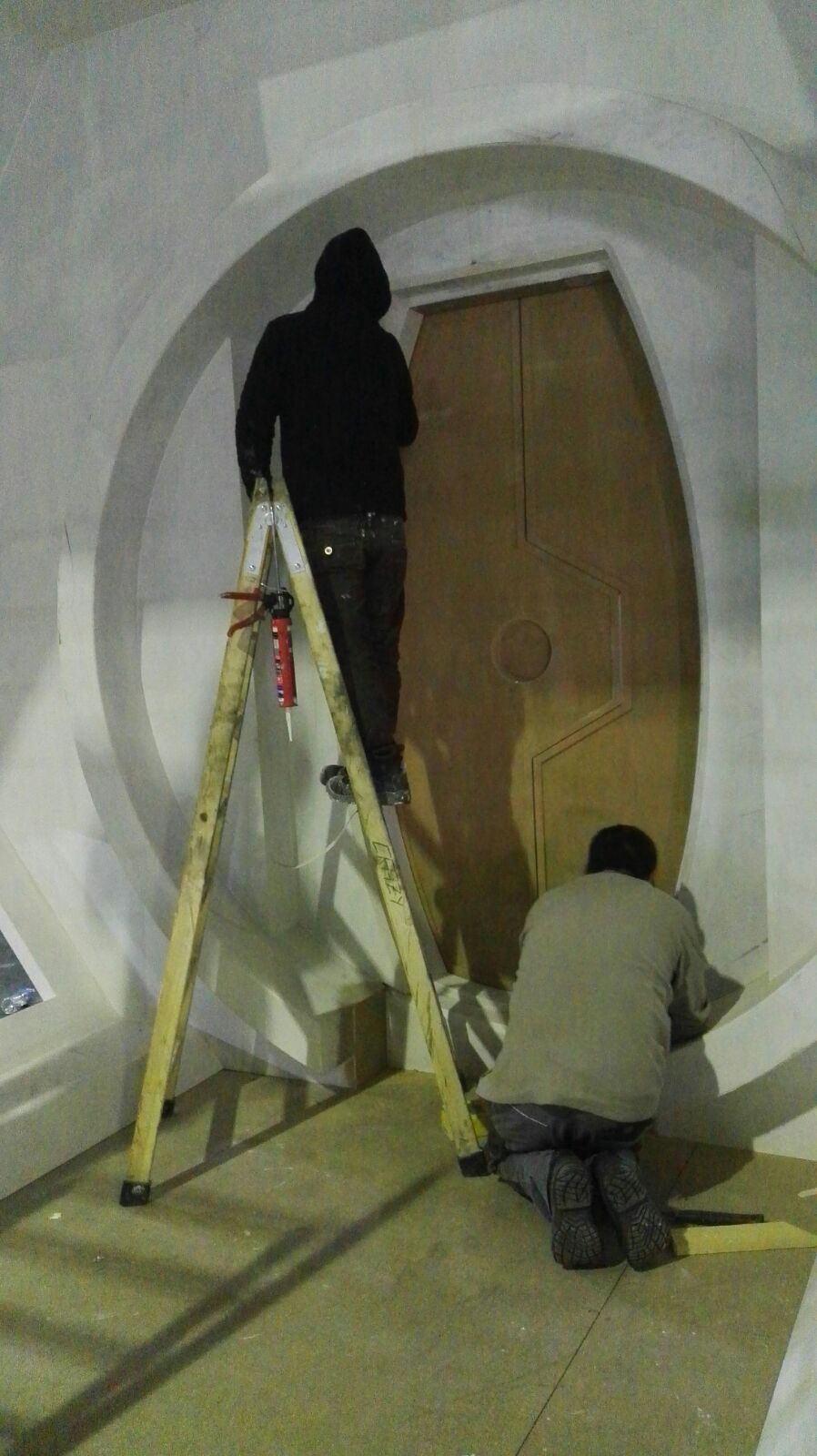 Dos hombres están arrodillados frente a una puerta mientras están de pie en una escalera.
