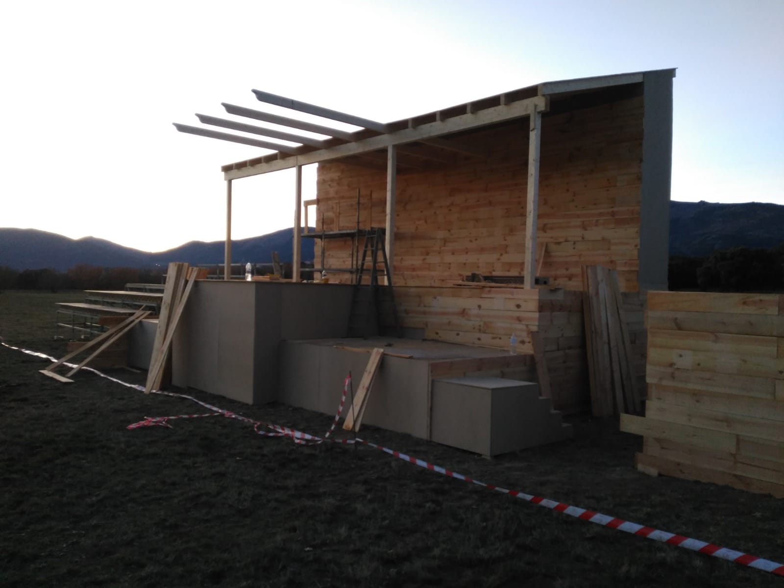 Se está construyendo una estructura de madera en un campo con montañas al fondo.
