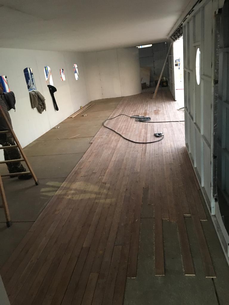 Una habitación larga con suelo de madera y una escalera.