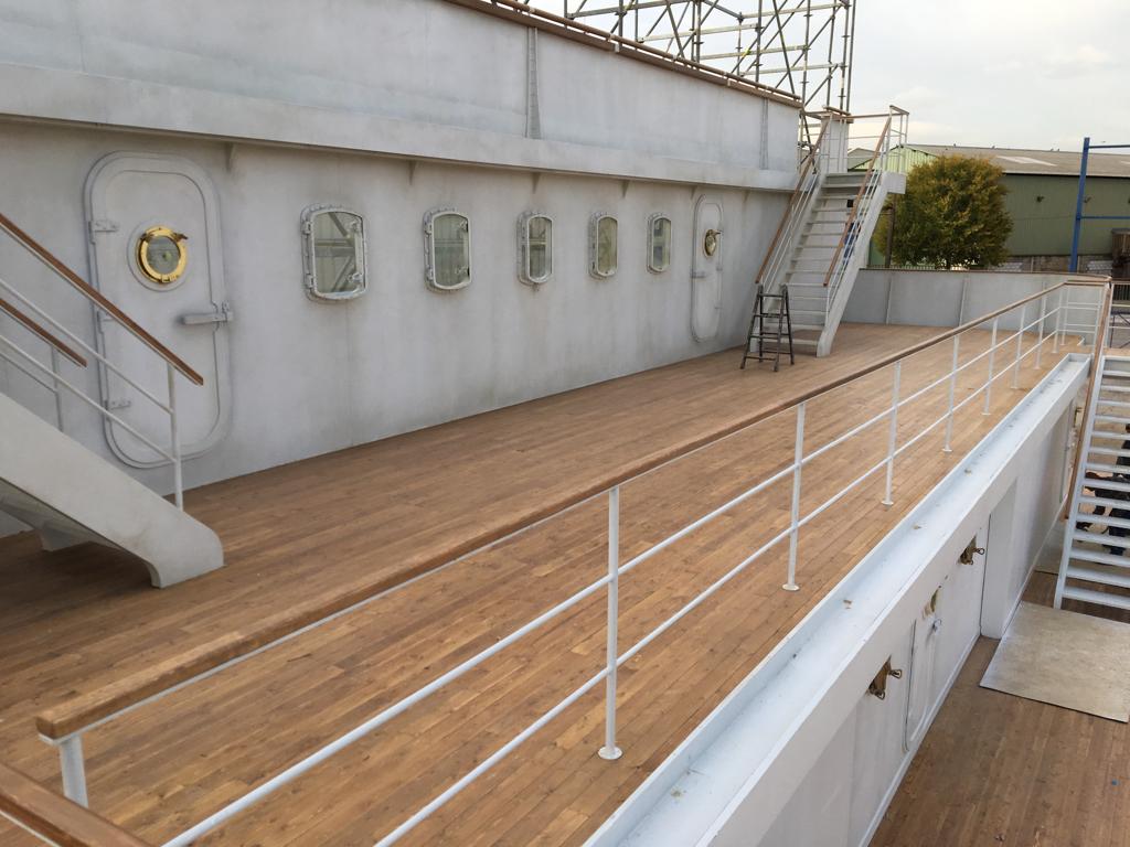 Una terraza de madera con escaleras y una barandilla blanca.