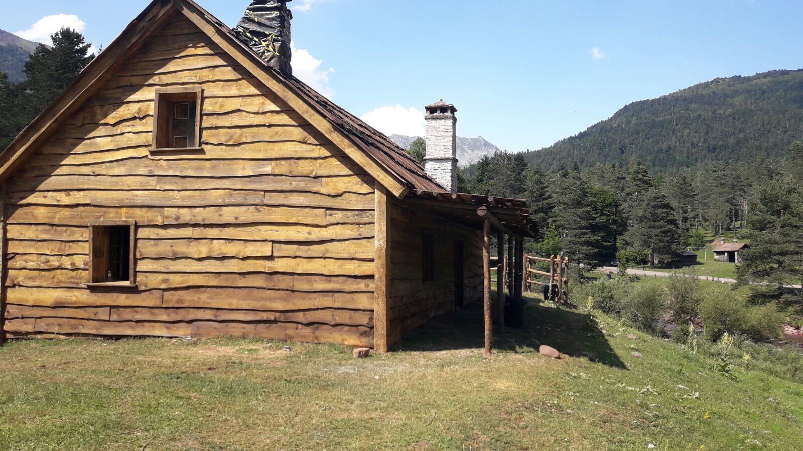 Una pequeña casa de madera en medio de un campo con montañas al fondo.