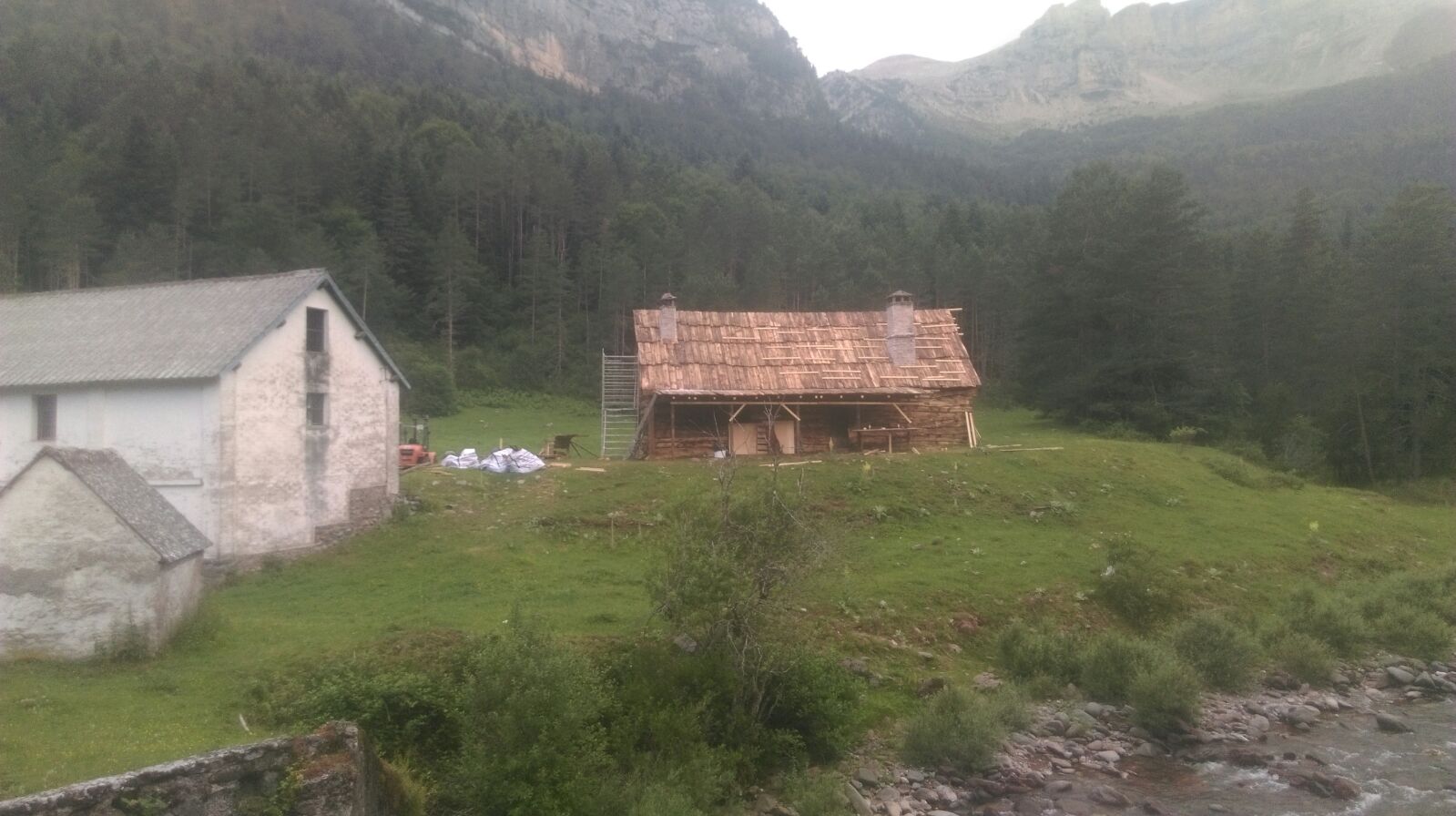 Una pequeña casa está situada en la cima de una colina cubierta de hierba al lado de un río.