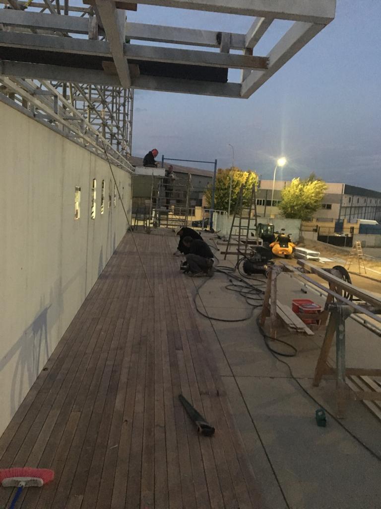 Un hombre está arrodillado sobre una plataforma de madera frente a un edificio en construcción.