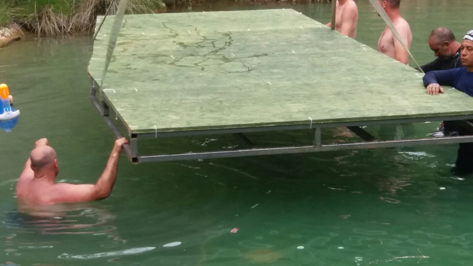 Un grupo de hombres lleva un gran trozo de madera en el agua.