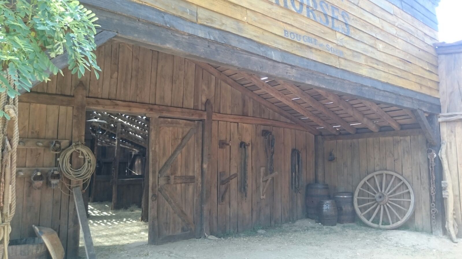 Un edificio de madera con una rueda de carreta delante de él.
