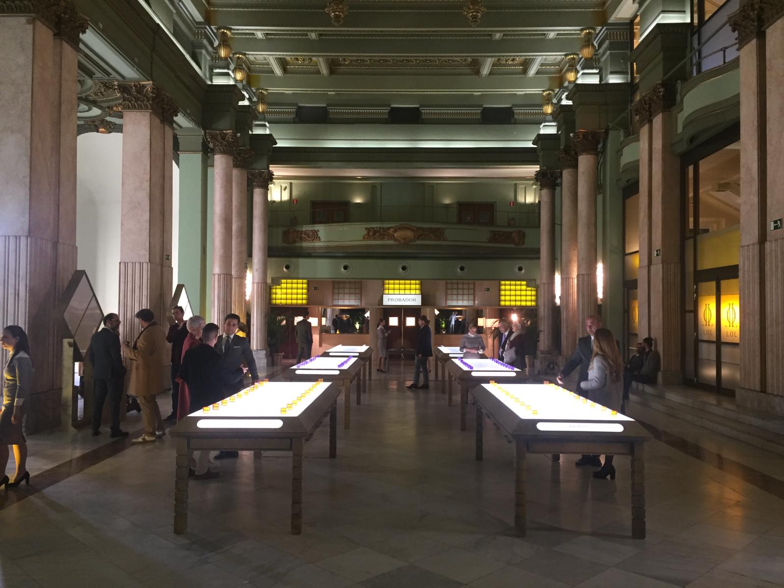 Un grupo de personas están de pie alrededor de mesas en una sala grande.