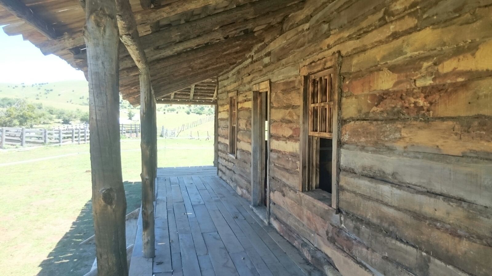 Una cabaña de troncos con un porche y una valla al fondo.