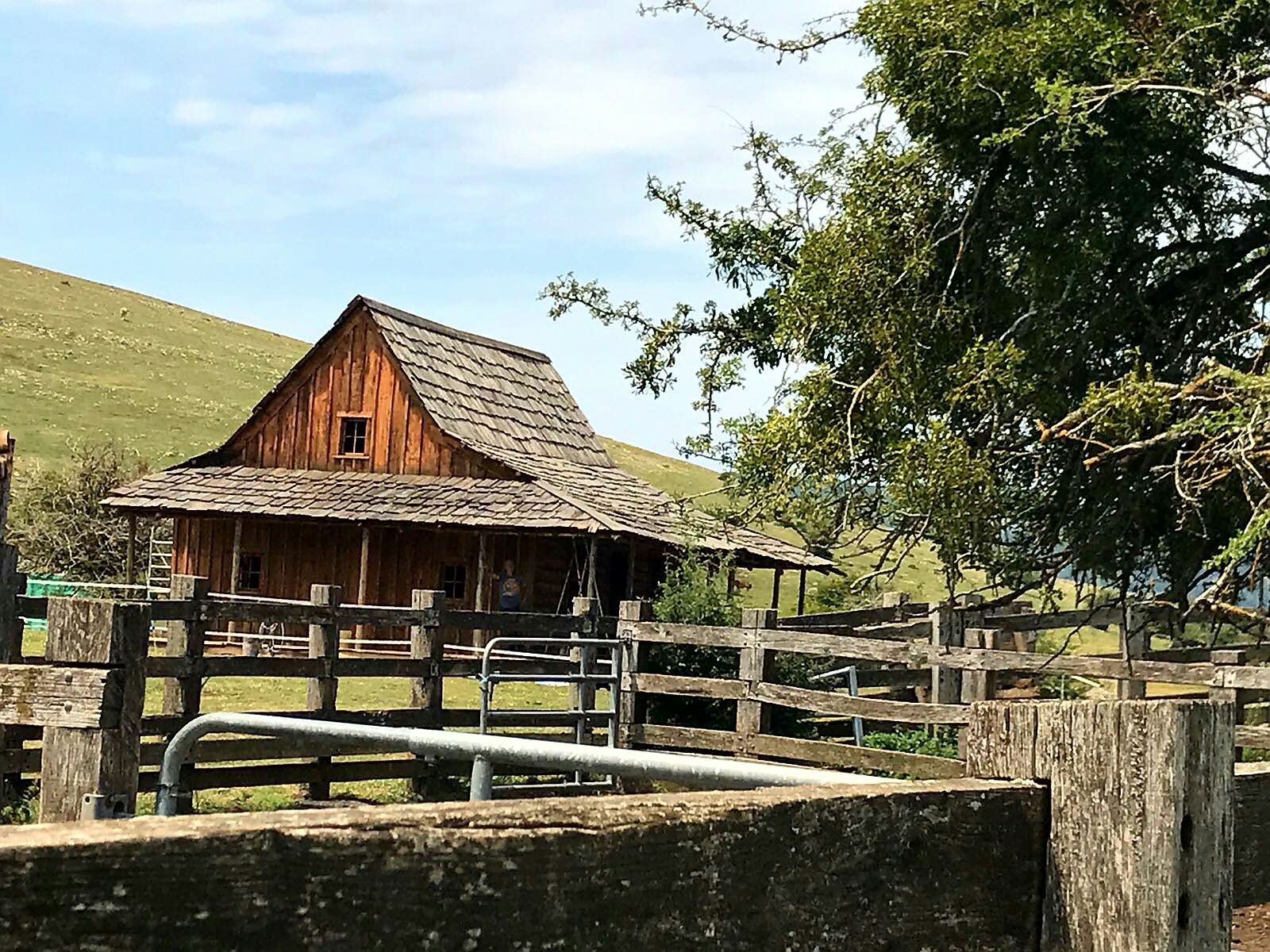Un granero de madera con techo de paja y una valla alrededor.