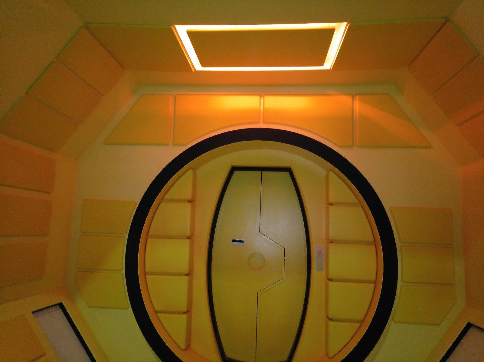 Una habitación amarilla con una puerta redonda y una luz cuadrada encima.