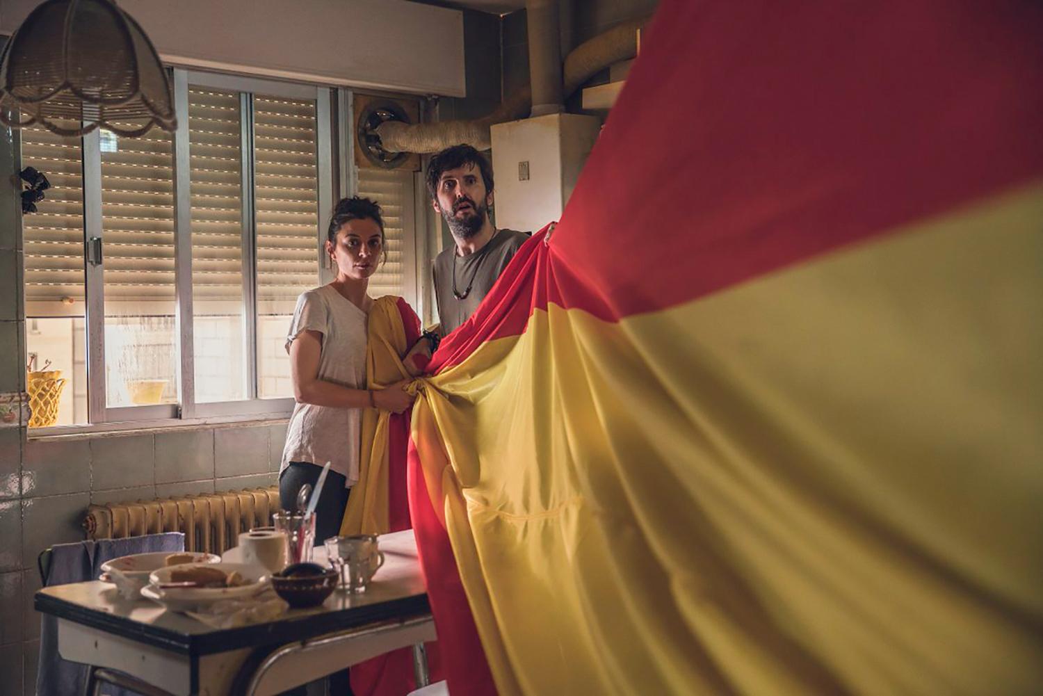 Un hombre y una mujer sostienen una bandera española en una cocina.