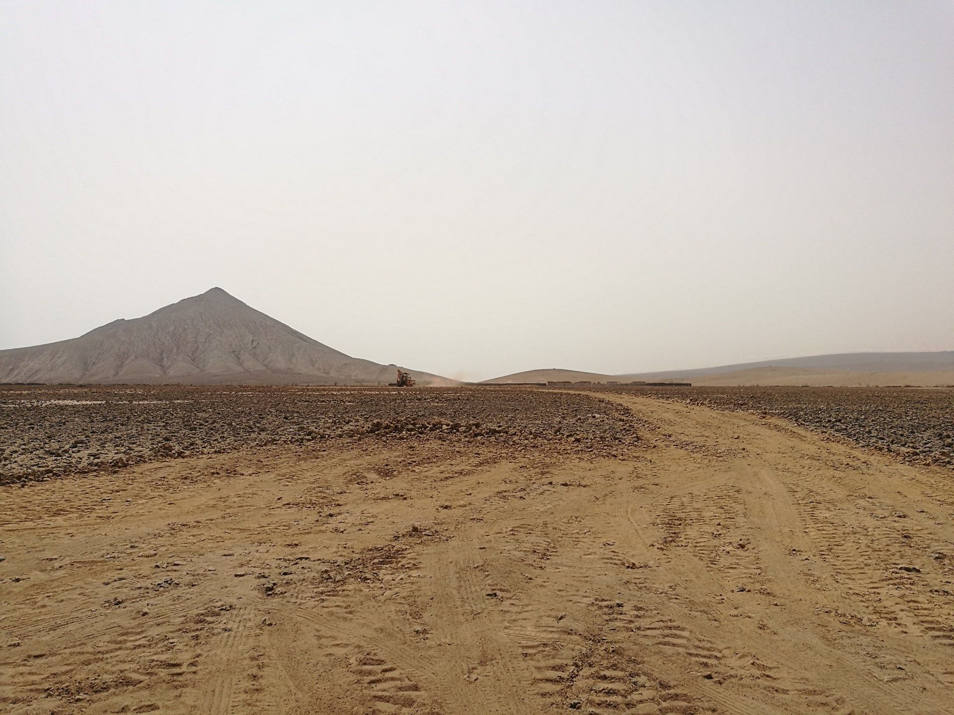 Un camino de tierra en el desierto con una montaña al fondo
