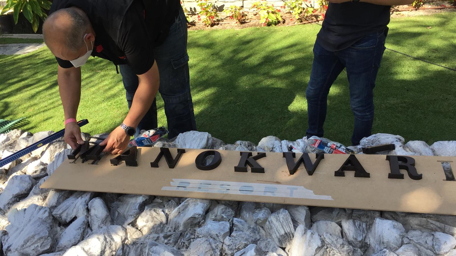 Dos hombres están trabajando en un cartel que dice Manokwar.