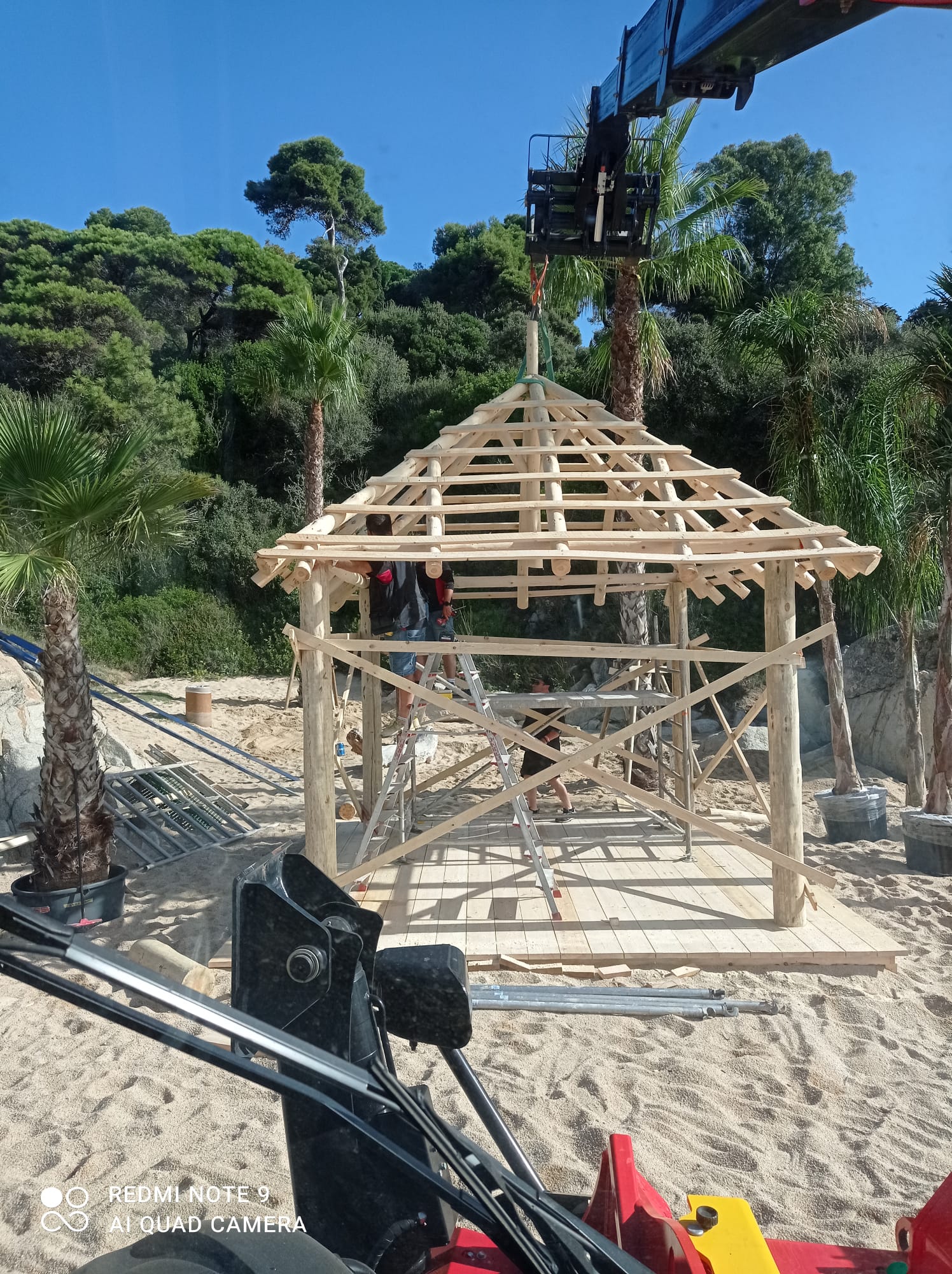 Una grúa está levantando una estructura de madera en una playa.