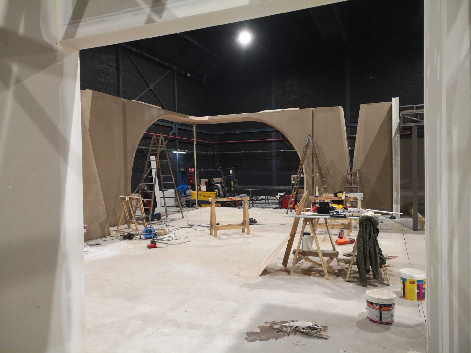 Una habitación grande con muchos andamios de madera y cubos de pintura.