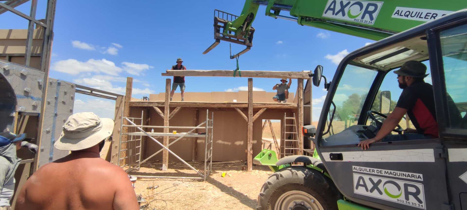 Un hombre está de pie junto a una carretilla elevadora verde en un sitio de construcción.