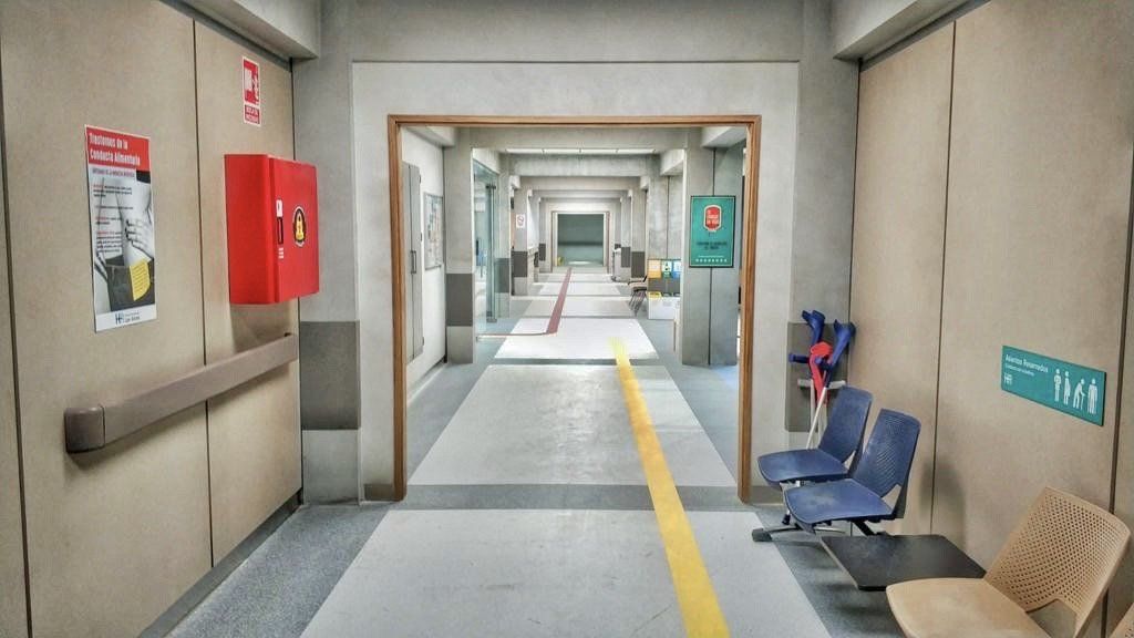 Un largo pasillo en un hospital con sillas y un extintor de incendios.