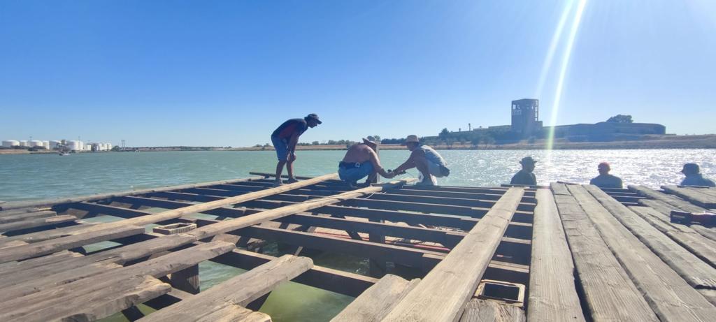 Un grupo de personas está de pie en un muelle de madera con vistas a un cuerpo de agua.