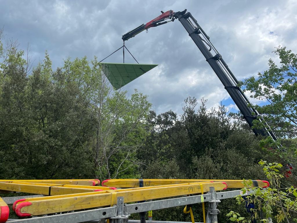 Una grúa está levantando un objeto verde sobre una estructura de madera.