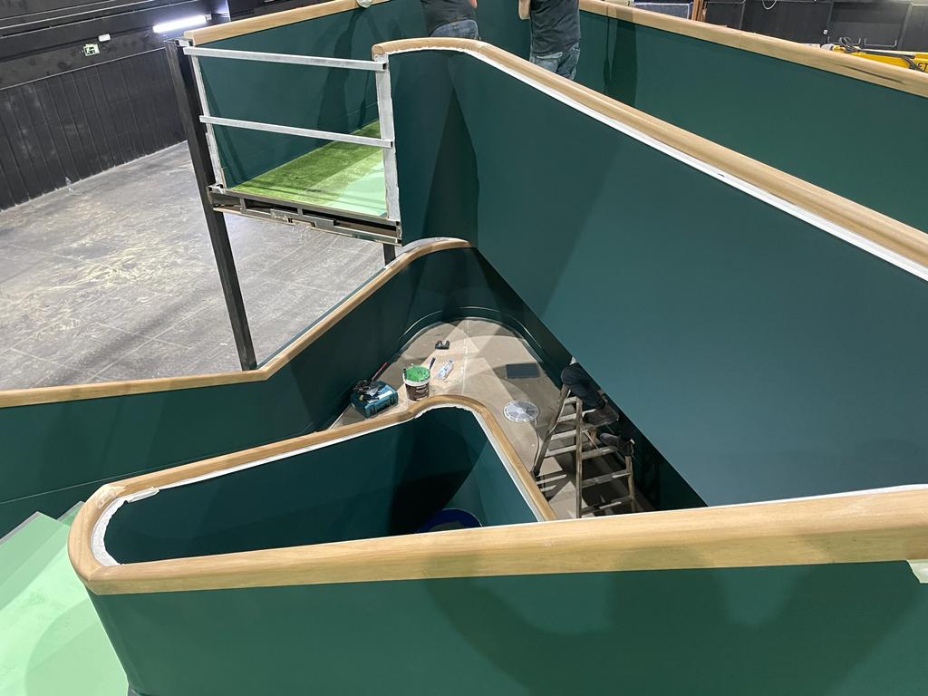 Una vista aérea de un laberinto con paredes verdes y barandillas de madera.