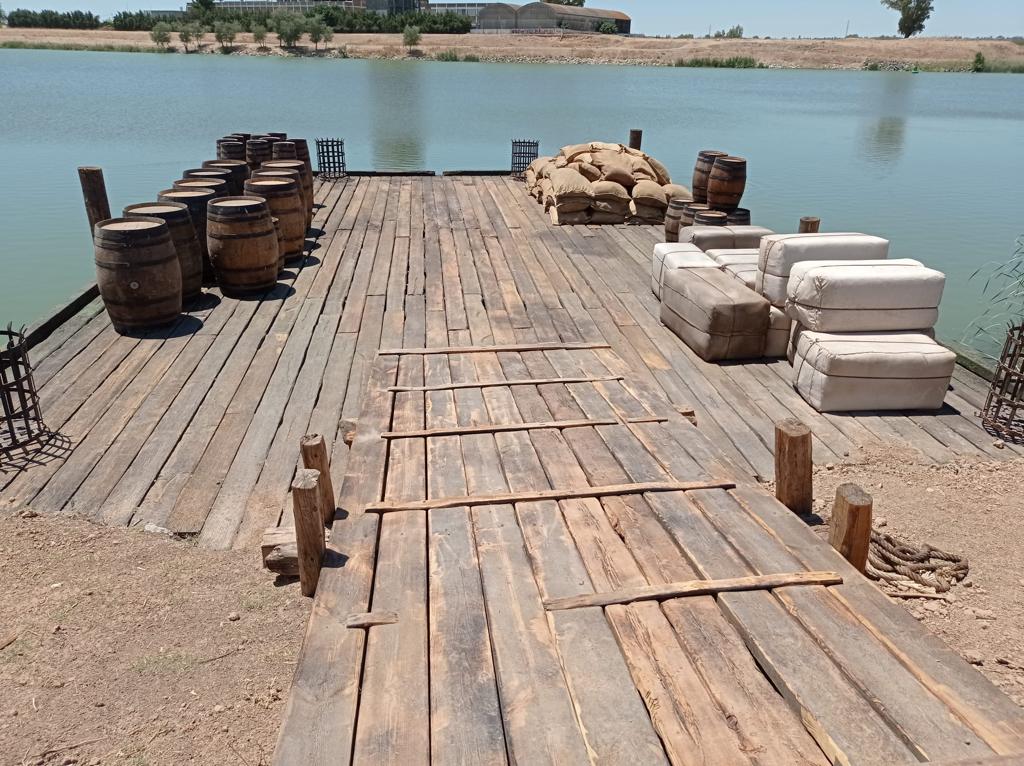 Un muelle de madera con barriles y bolsas encima.