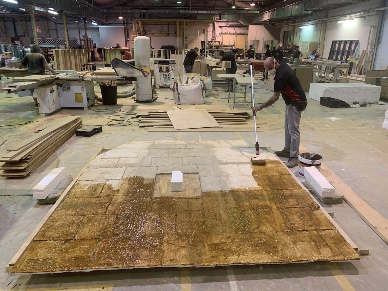 Un hombre está pintando un gran trozo de madera en una fábrica.