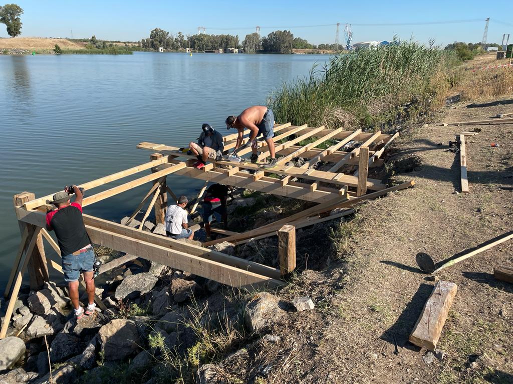 Un grupo de personas está trabajando en una estructura de madera al lado de un lago.