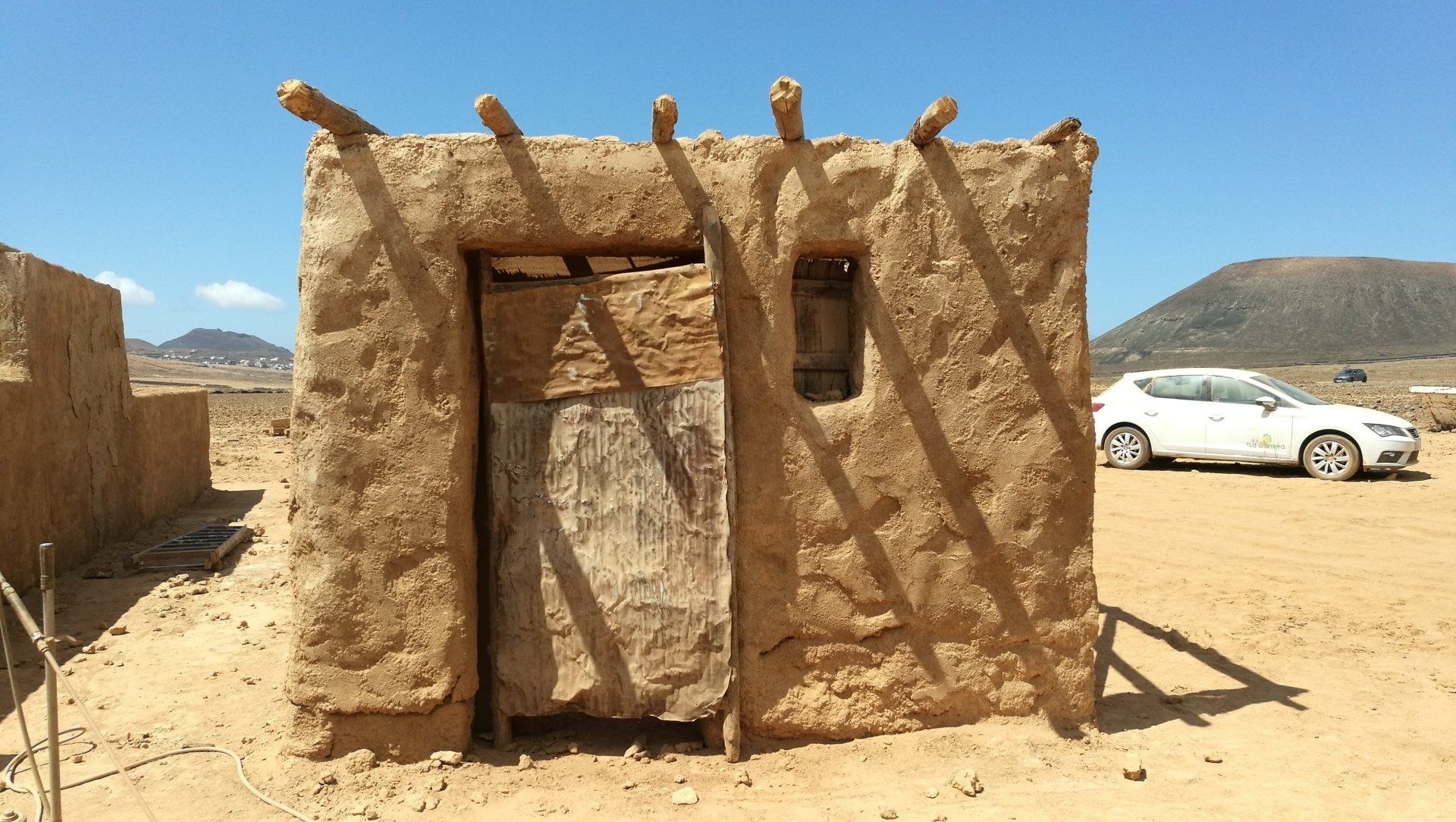Un coche blanco está aparcado delante de un edificio en el desierto.