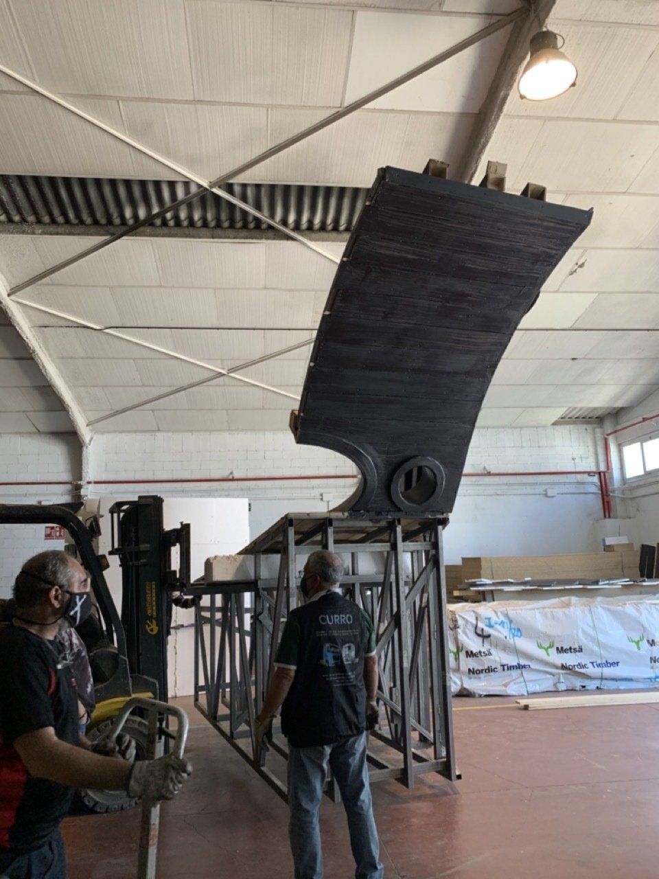Dos hombres están trabajando en una gran pieza de metal en un almacén.