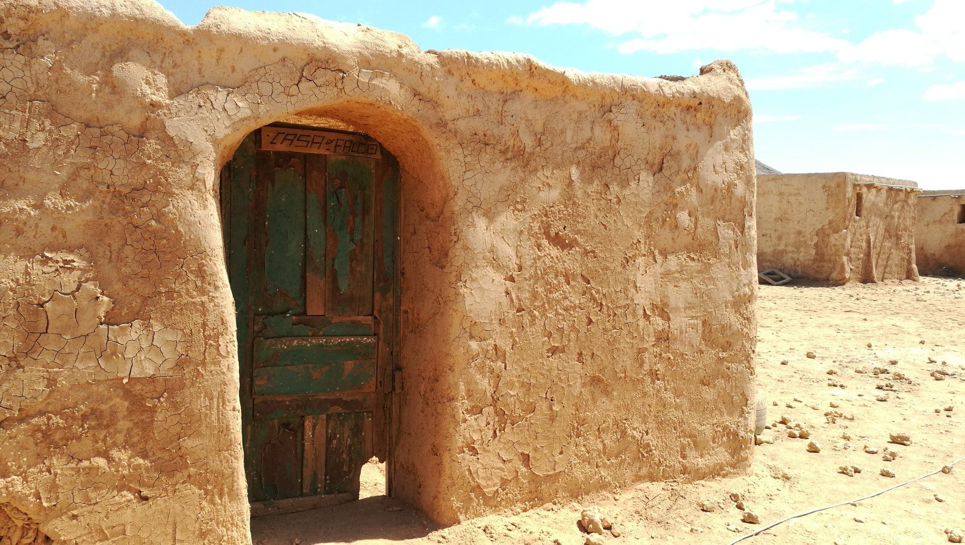 Un edificio de ladrillo con una puerta verde en medio del desierto.