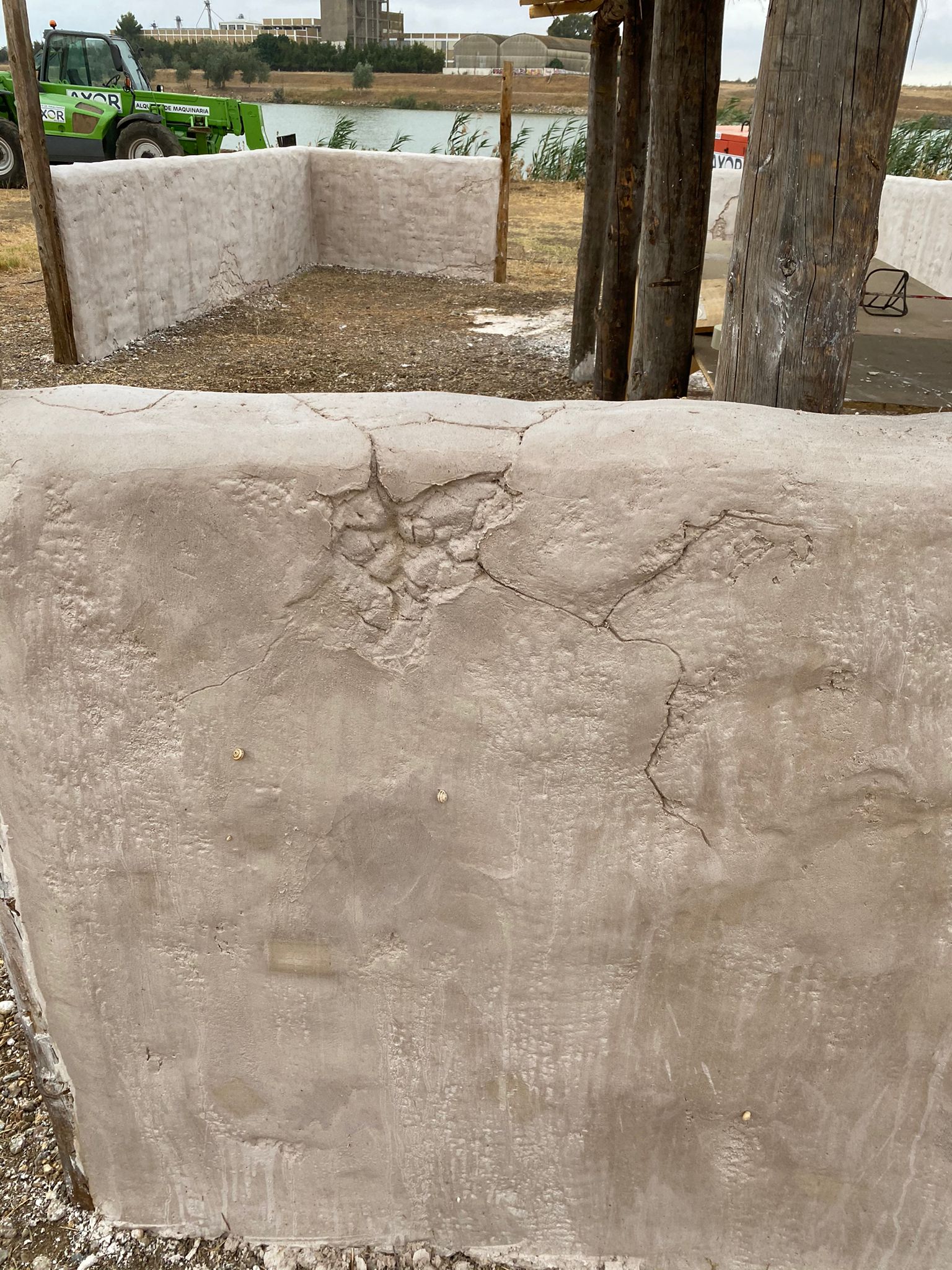 Un muro de hormigón con un árbol al fondo y un tractor verde al fondo.