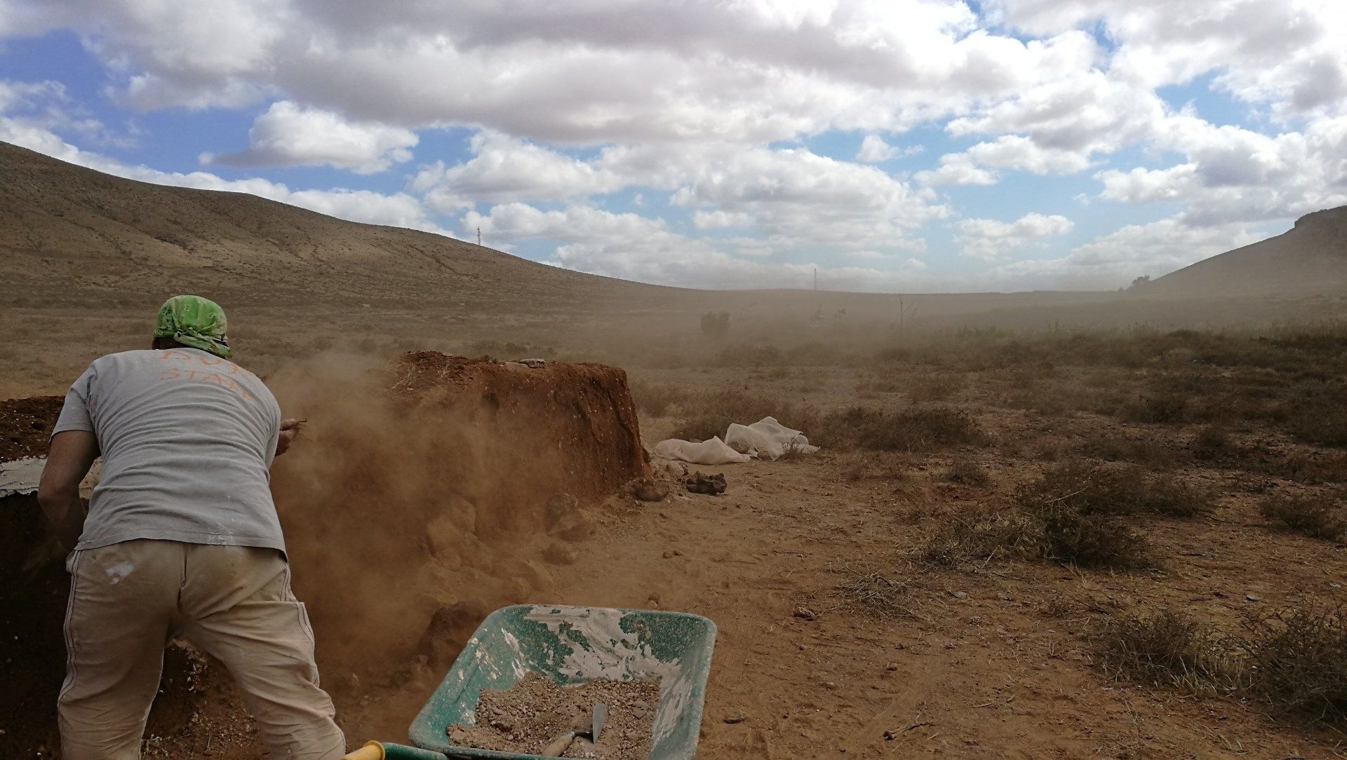 Un hombre empuja una carretilla llena de tierra en el desierto.