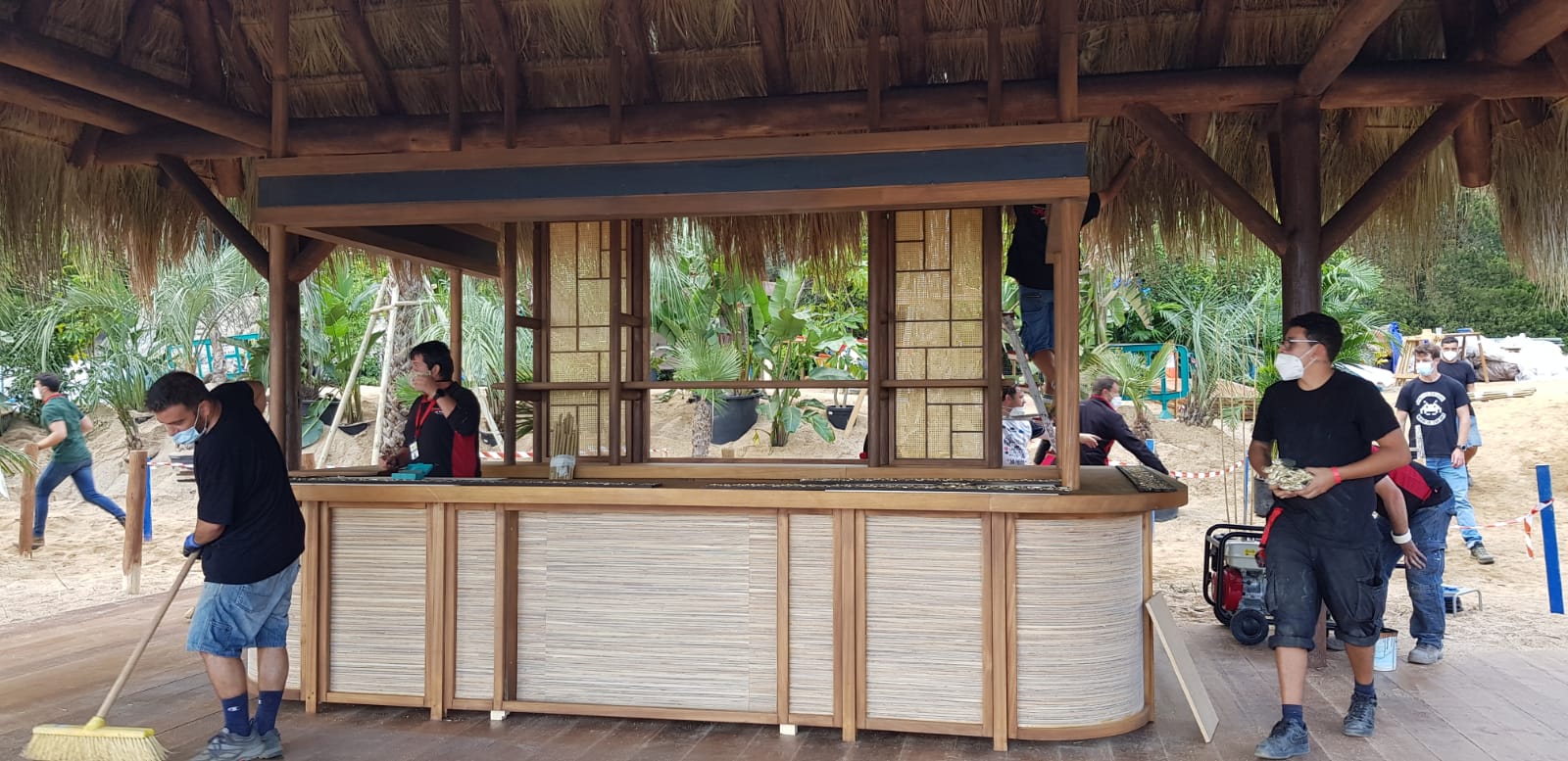 Un grupo de personas está trabajando en una estructura de madera bajo un techo de paja.