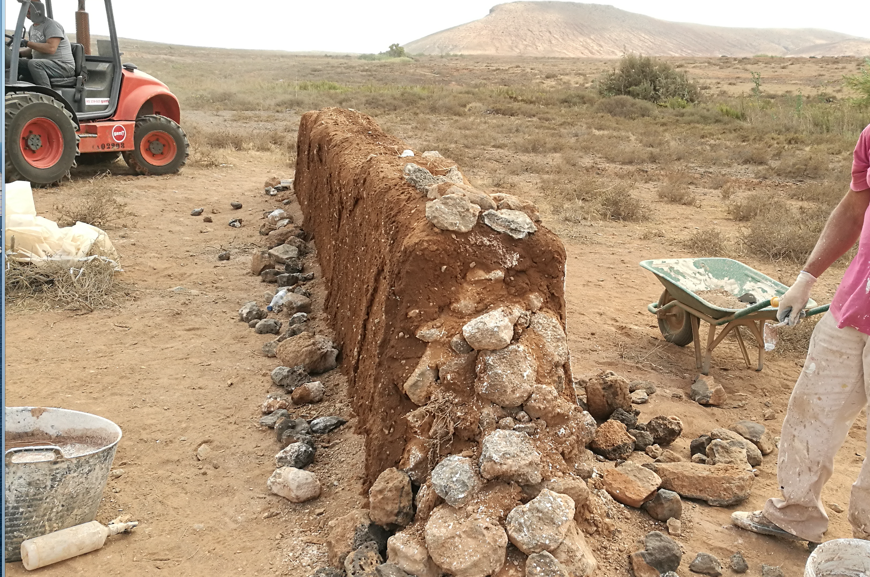 Un hombre con una camisa rosa está de pie junto a una pila de rocas.