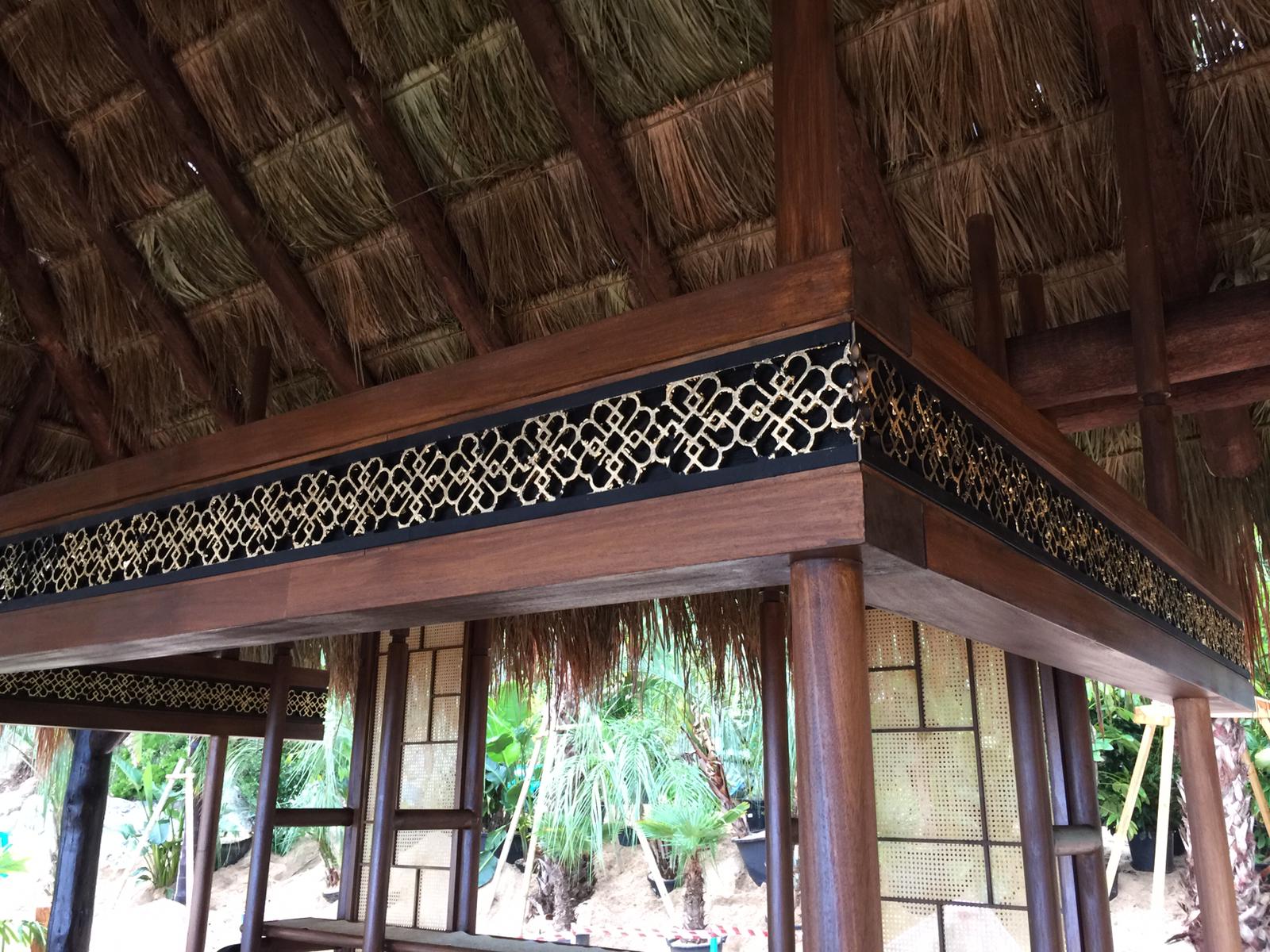 Una estructura de madera con techo de paja está rodeada de árboles.