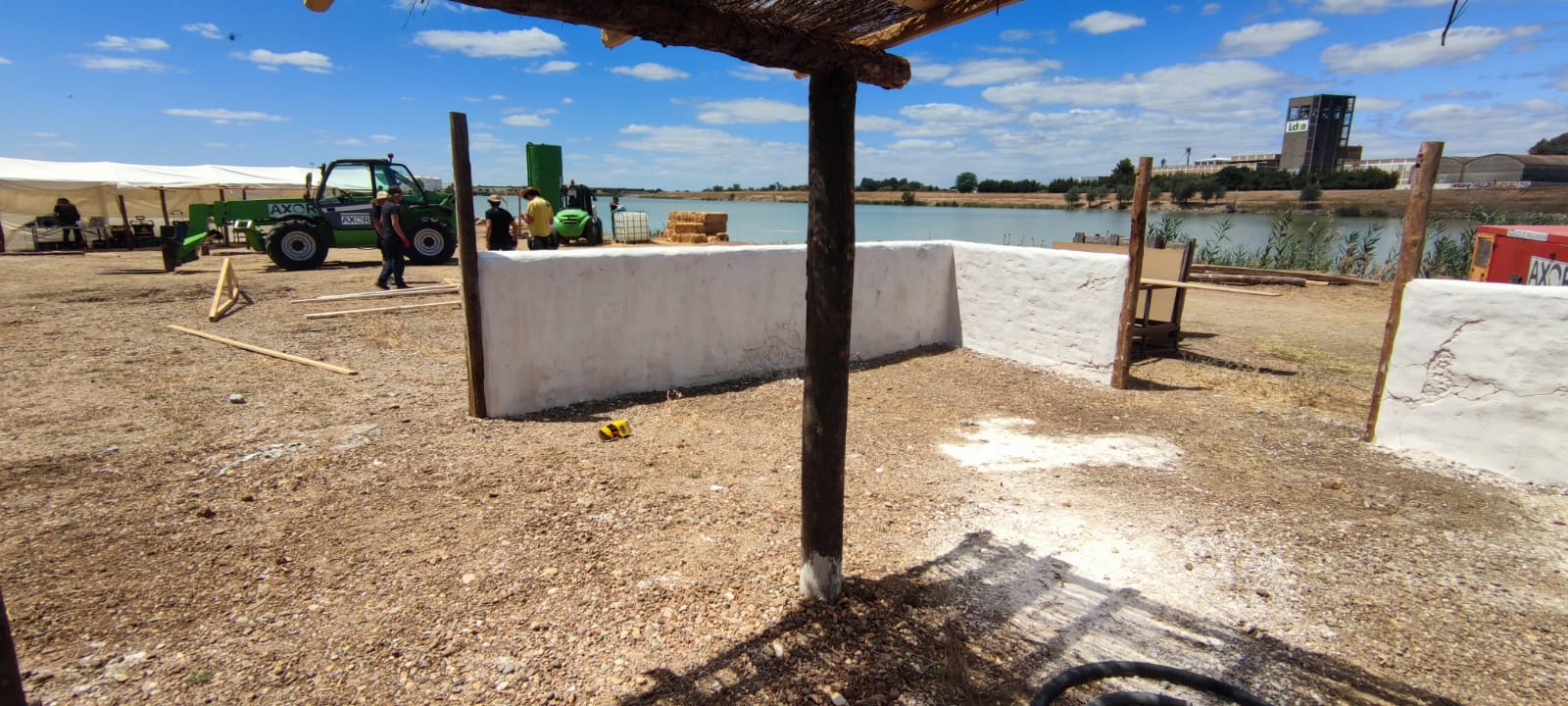 Un tractor verde está estacionado en un campo de tierra al lado de un cuerpo de agua.