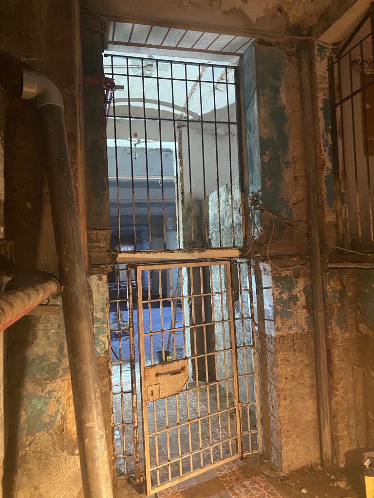 Una habitación sucia con una puerta de metal y una ventana.