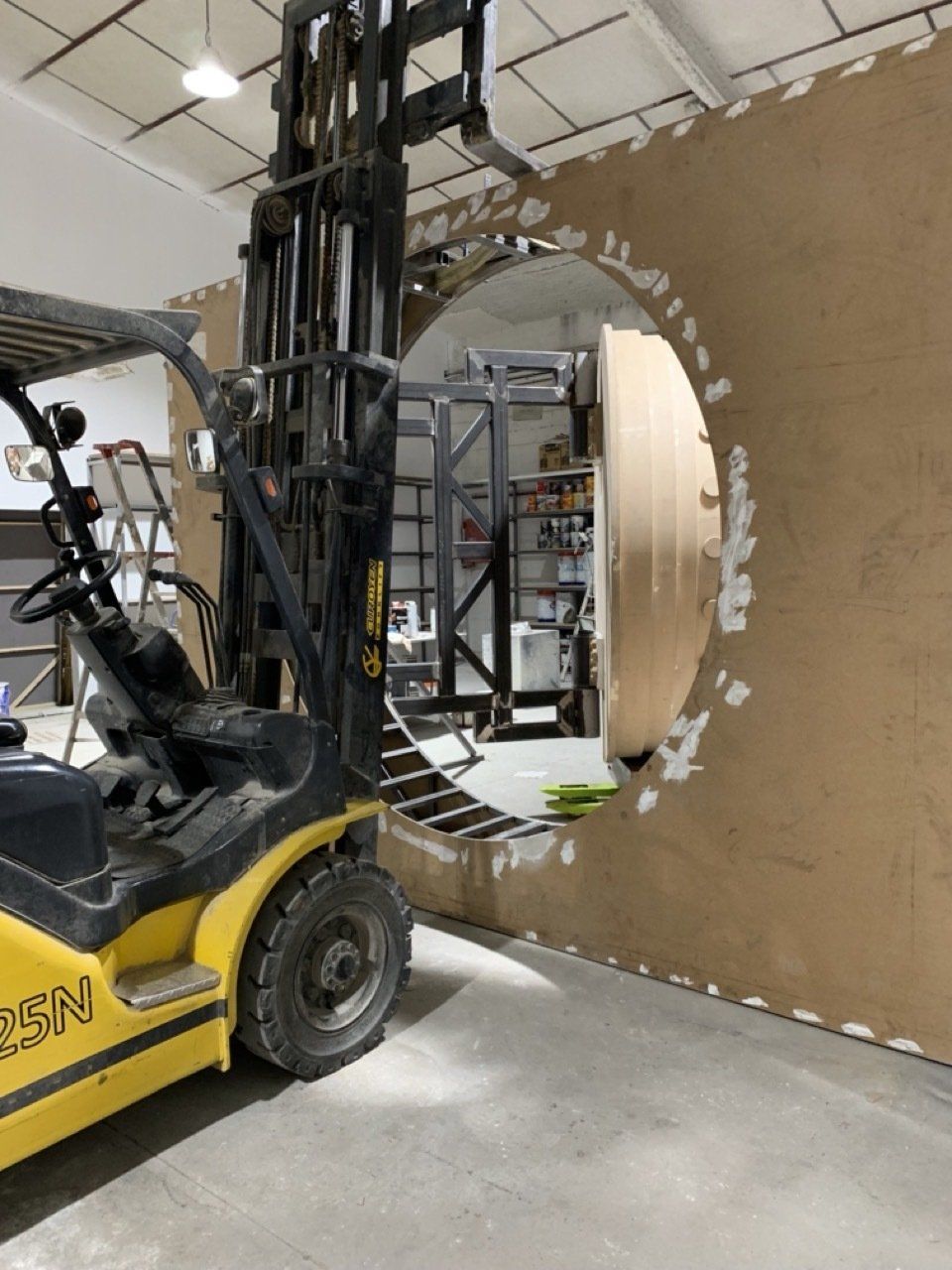 Una carretilla elevadora está levantando un gran trozo de madera y colocándolo en un agujero en una pared.