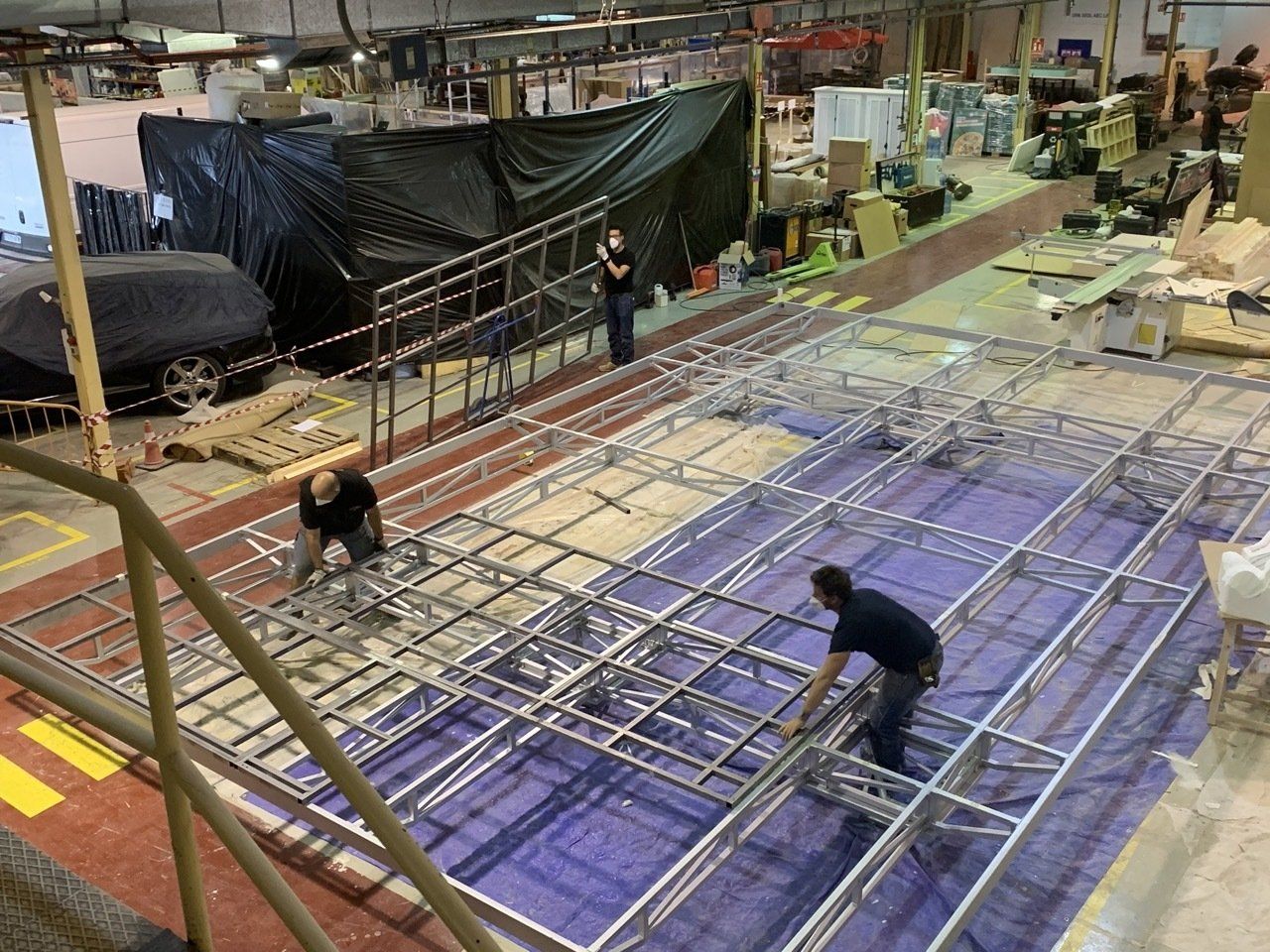 Dos hombres trabajan en una estructura metálica en una fábrica.