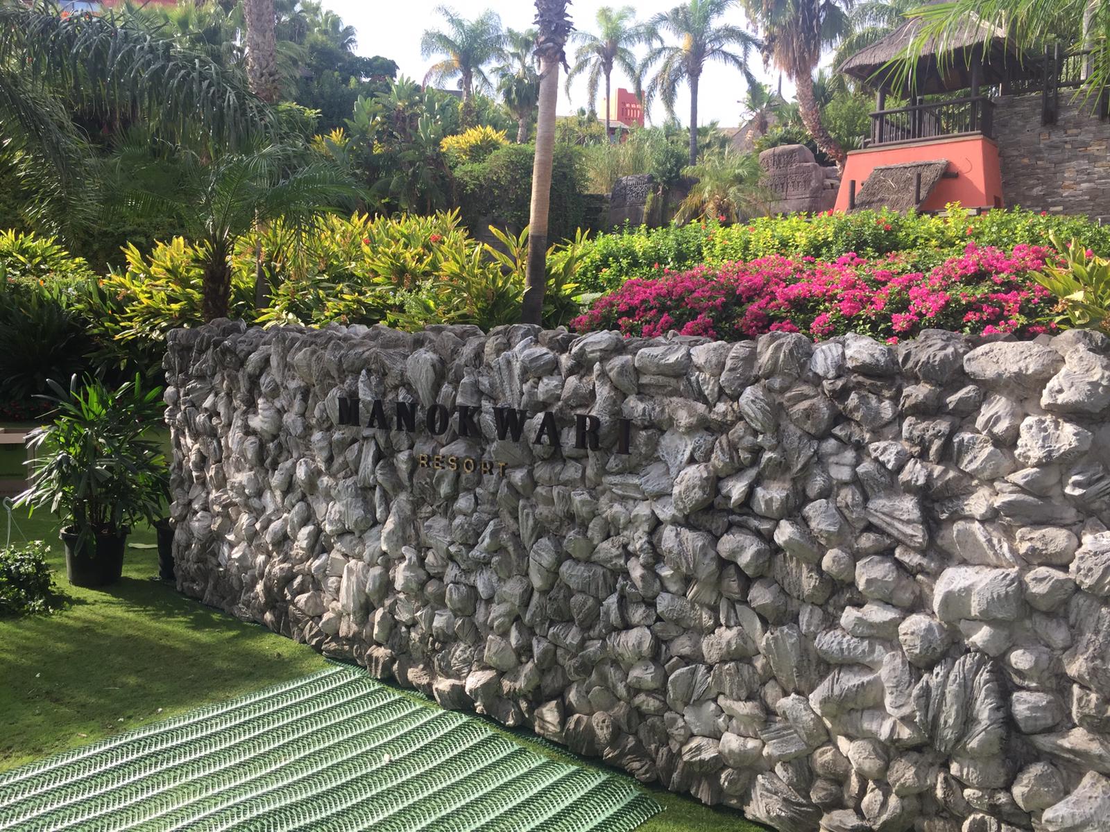 Un gran muro de piedra con un cartel en un jardín.