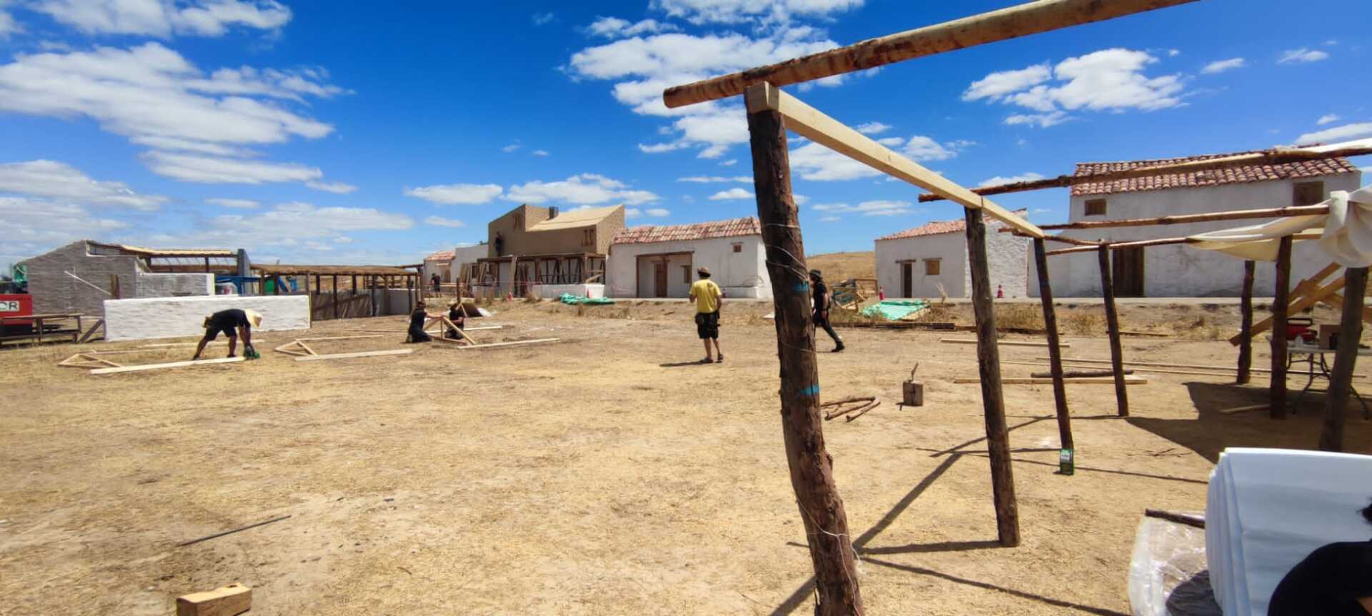 Un grupo de personas está trabajando en un edificio en un campo de tierra.