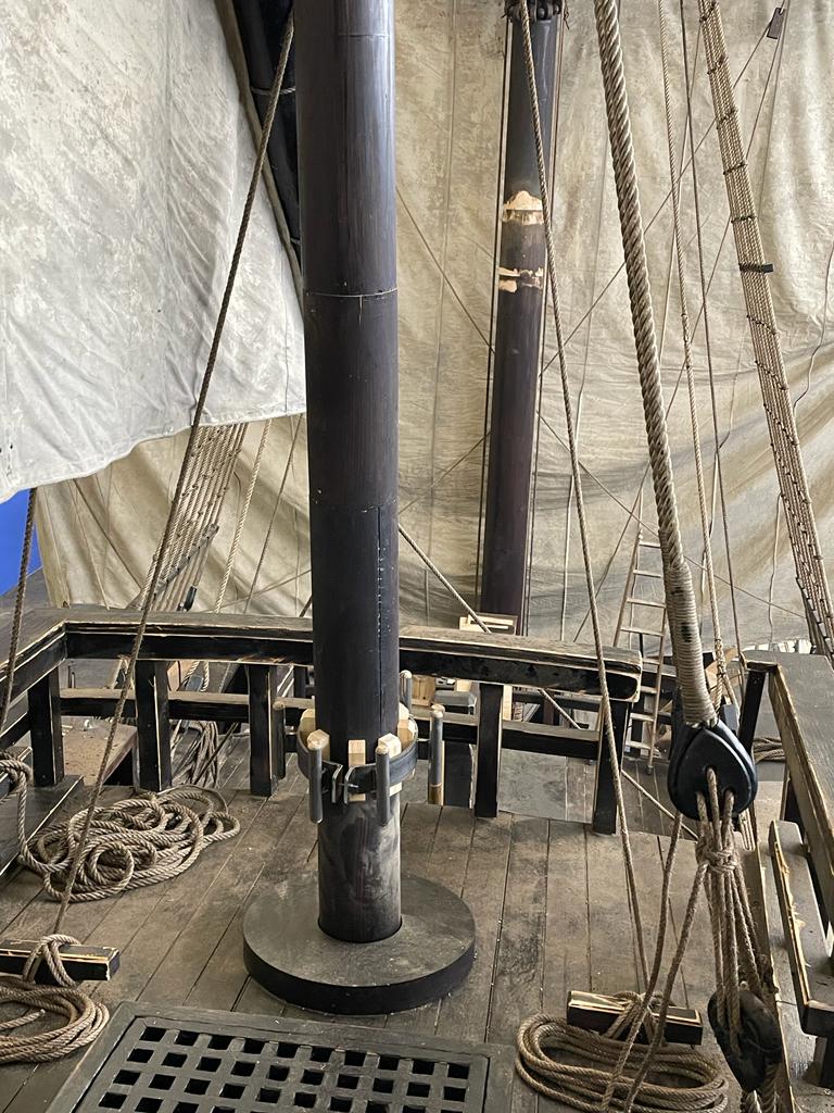 Un primer plano de una cubierta de madera de un barco con cuerdas y postes.